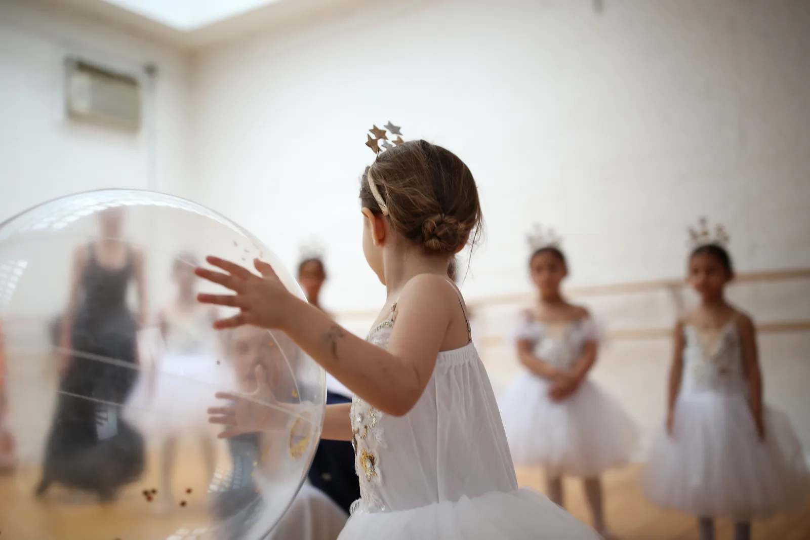 Child in a star crown reaching for a large clear balloon during rehearsal