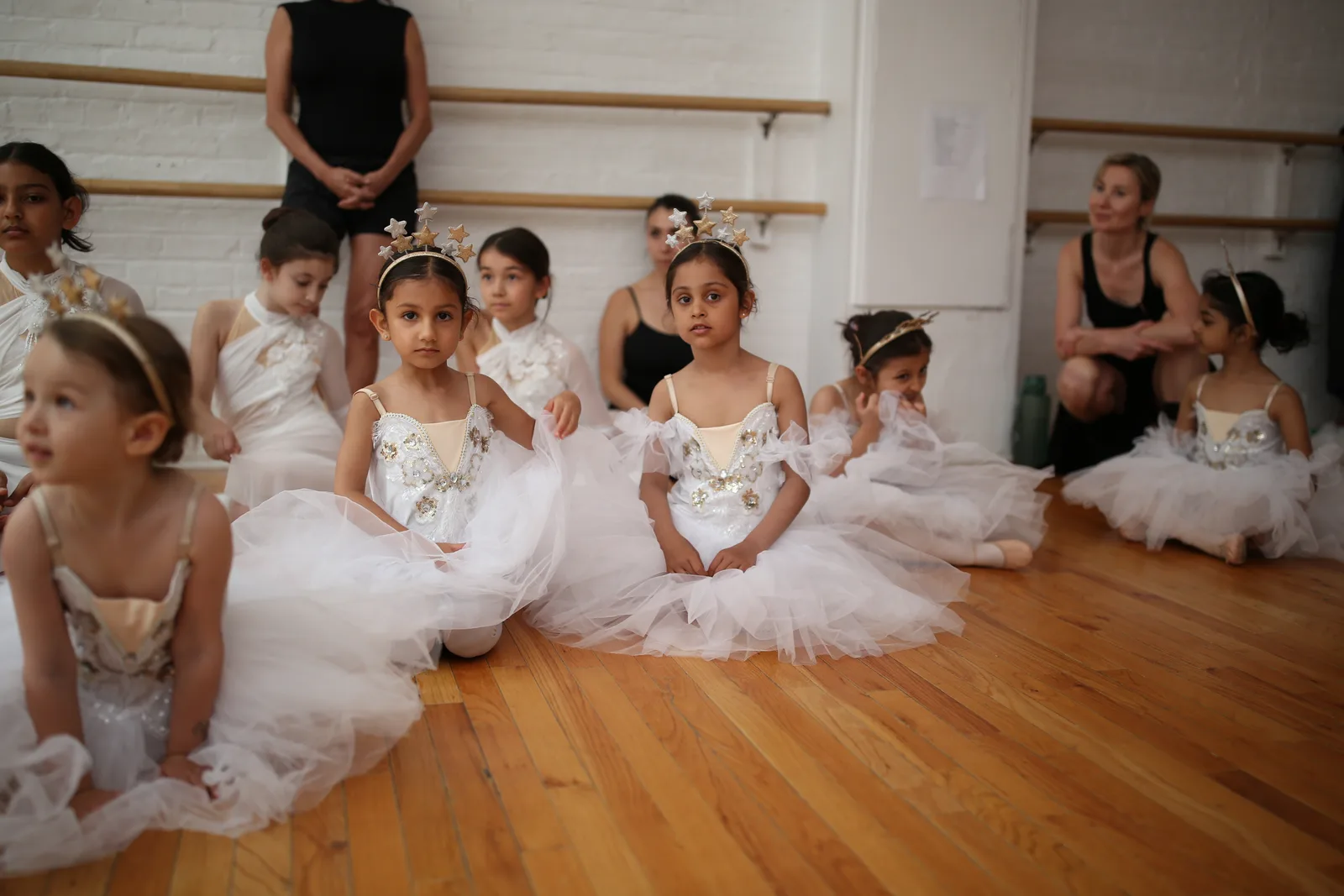 Group of young dancers in white tutus sitting together on the studio floor