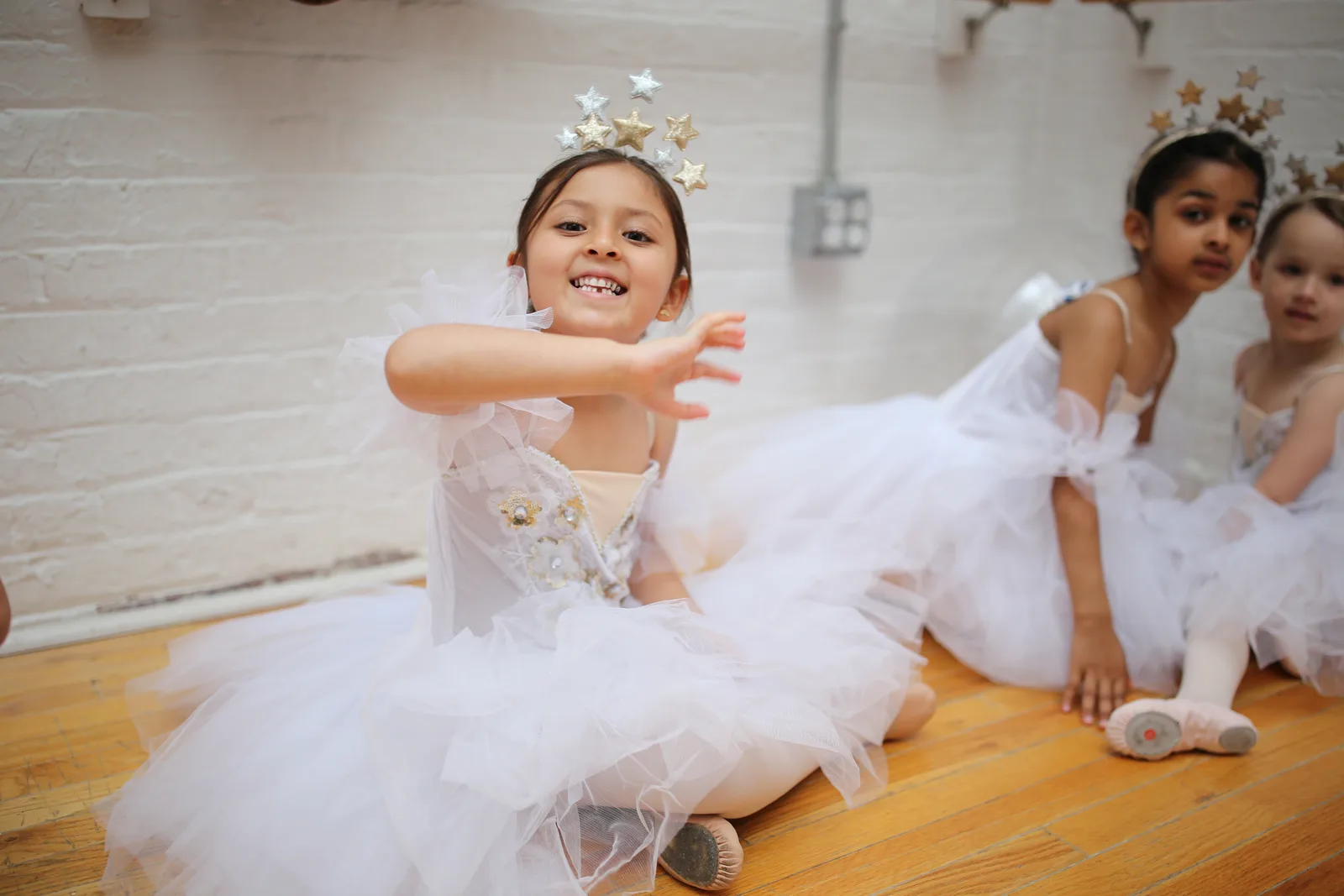 Young girl in a white tutu and star crown reaching toward the camera during dress rehearsal at Streetcar Studio