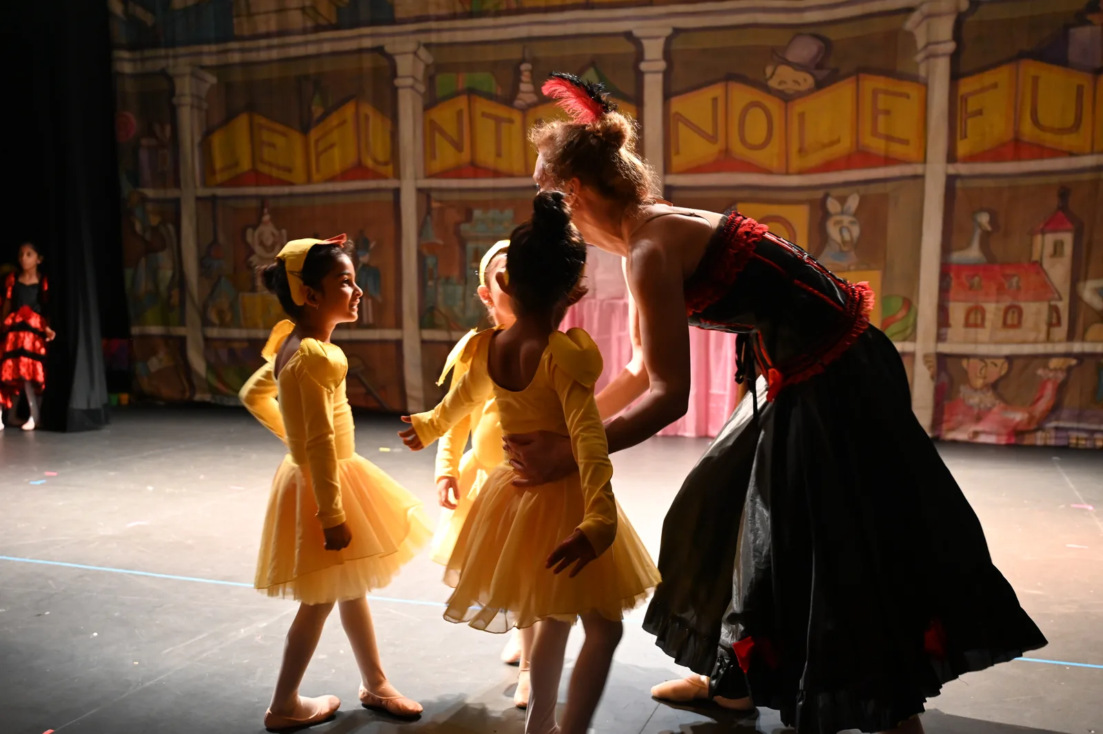 Teacher in costume guiding young dancers in yellow on stage