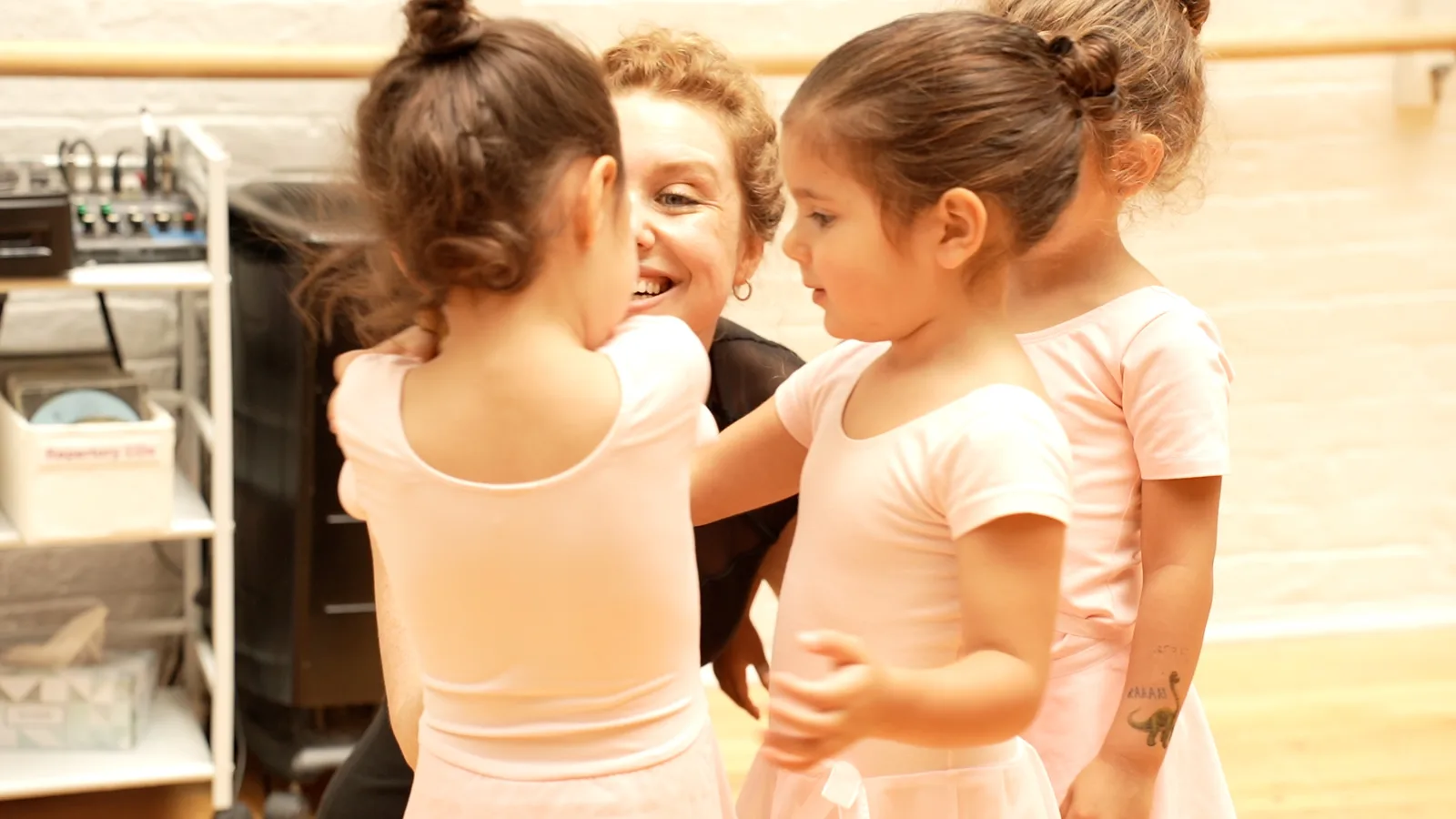 Teacher laughing with two children in pink leotards in the studio