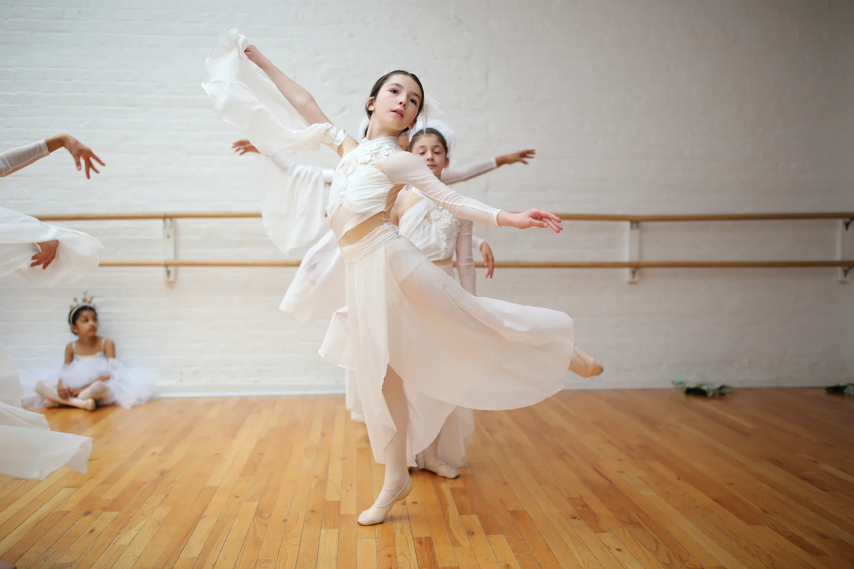 A student turning mid-phrase in a flowing white costume at dress rehearsal