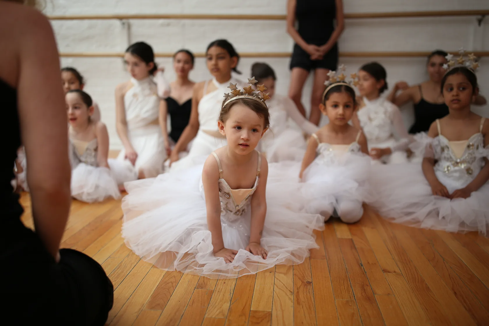 Students in tutus and star crowns sitting on the studio floor between runs