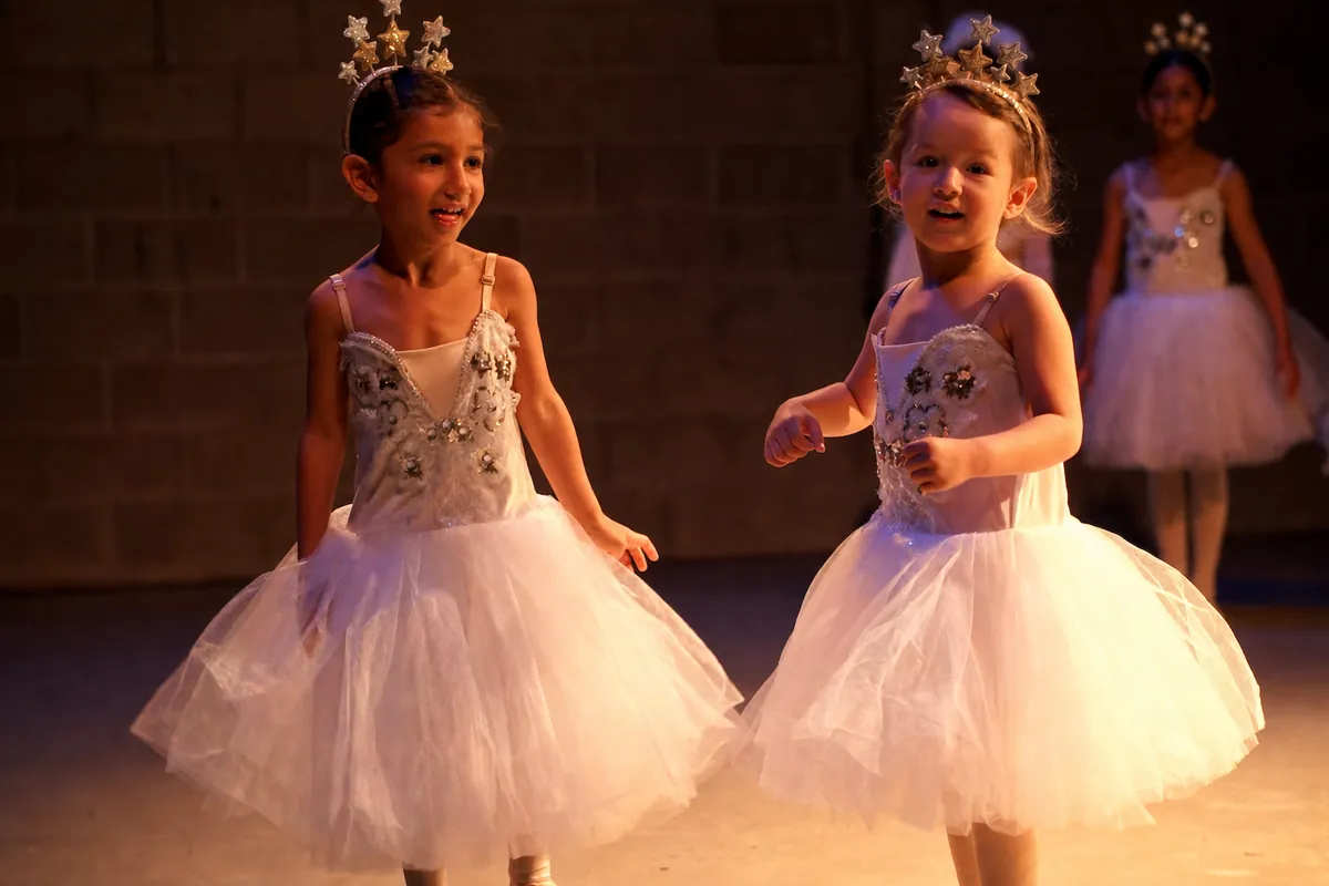 Two students in star crowns and white tutus laughing mid-scene