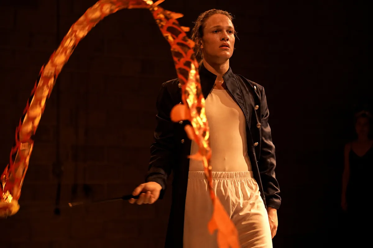 A performer drawing an arc of fire-coloured ribbon through the air