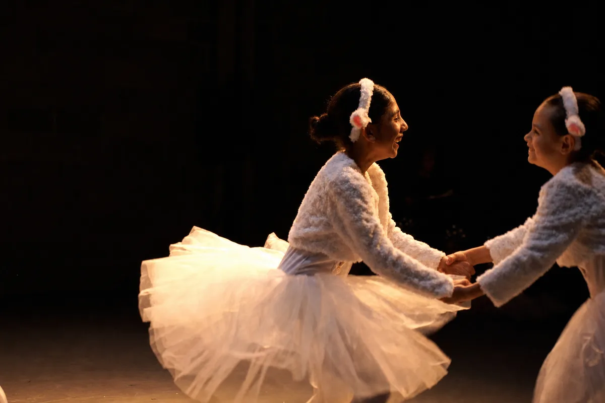 Two students in white tutus and fluffy ear headbands spinning hand in hand