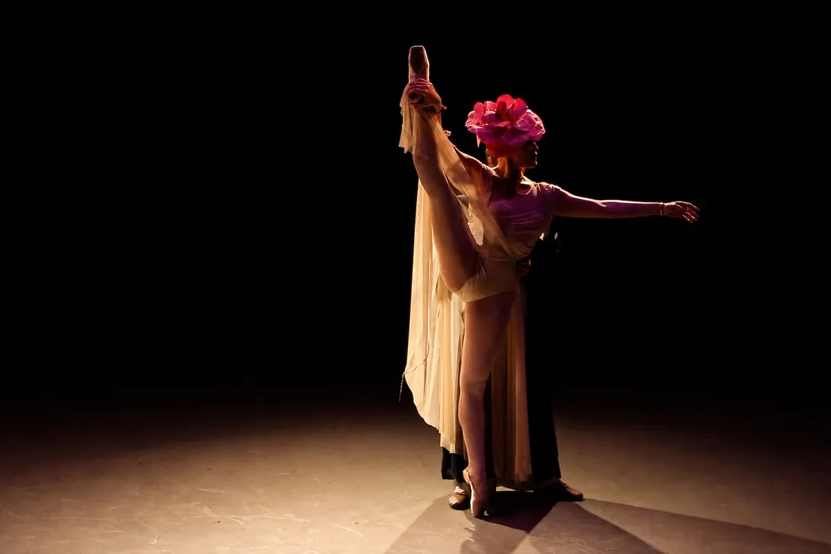 Two performers silhouetted in a single spotlight, lifting the rose