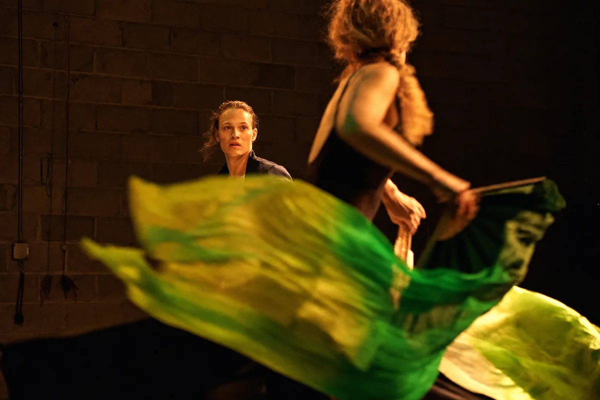 A performer watching as a painted green silk sweeps across the stage